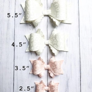 Puede incluir: Cuatro lazos de tela blanca y rosa con bordes festoneados. Los lazos están dispuestos en una línea vertical de mayor a menor. Los lazos miden 5,5 pulgadas, 4,5 pulgadas, 3,5 pulgadas y 2,5 pulgadas.