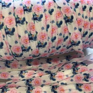 May include: A roll of white elastic with a pink and blue floral print. The elastic is folded and rolled up, and the floral print is visible on the outside of the roll.
