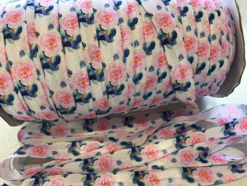 May include: A roll of white elastic with a pink and blue floral print. The elastic is folded and rolled up, and the floral print is visible on the outside of the roll.