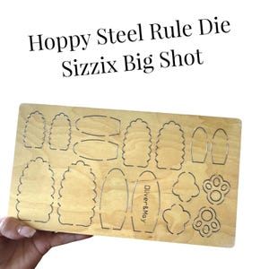 May include: A wooden die-cutting board with various shapes, including beehives, ovals, and paw prints. The board has the text "Hoppy Steel Rule Die Sizzix Big Shot" and the brand name "Oliver & May".