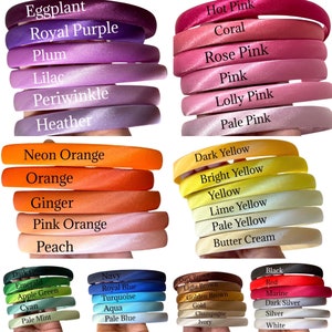 May include: A collection of colourful satin headbands in various shades of pink, orange, yellow, blue, green, and red. The headbands are arranged in rows, with each row featuring a different colour.