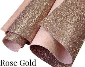 Puede incluir: Hojas de fieltro de lana pura con purpurina oro rosa. La imagen muestra varias hojas de fieltro con un acabado de purpurina oro rosa, con un reverso rosa claro. El fieltro está enrollado y en capas, mostrando la textura y las variaciones de color.