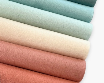 Puede incluir: Cinco rollos de tela de fieltro en varios tonos de azul, beige y marrón. El fieltro es un material suave y texturizado.