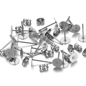 Può includere: Primo piano di un mucchio di dorsi di orecchini argentati. I dorsi sono in metallo e hanno un piccolo anello sul retro. Sono progettati per essere utilizzati con orecchini a perno.