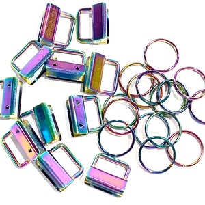 May include: A collection of iridescent rainbow-coloured metal hardware, including several rectangular fob clips with flat attachment points and multiple circular split rings, all featuring a metallic finish that shifts between purple, blue, and gold hues.