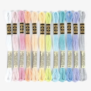 Puede incluir: Una colección de hilos de bordar DMC en una variedad de colores pastel. El hilo está cuidadosamente organizado, con cada madeja etiquetada con un número. Los colores incluyen blanco, rosa, melocotón, amarillo, verde, azul y lavanda. Las madejas miden aproximadamente 8 metros.