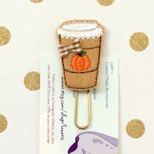 May include: A felt coffee cup bookmark with a pumpkin design and a gold paper clip. The bookmark is on a white background with gold glitter dots. The text on the card reads "LaAri's Custom Made Accessories" and "www.etsy.com/shop/laaris".