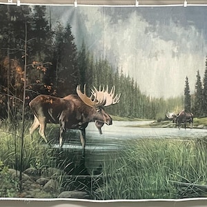 May include: A rectangular fabric panel featuring a printed landscape scene of two moose standing in a shallow lake surrounded by tall green grasses and a dense forest of pine trees under a cloudy sky. The fabric has a white border on all sides.