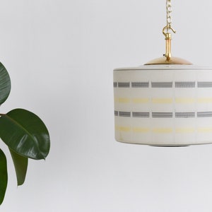 May include: A white pendant light with a brass chain and a geometric pattern of black and yellow lines.