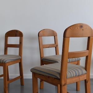 May include: Four wooden chairs with light brown frames and striped seat cushions. The chairs have a simple design with a curved top on the backrest. The seats feature a blue and beige striped pattern.