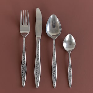 May include: Four silver-coloured pieces of cutlery: a fork, knife, and two spoons. The handles feature a textured, mosaic-like design. The utensils are displayed against a solid, reddish-brown backdrop.