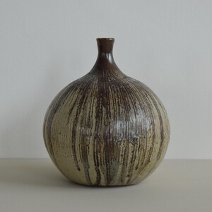 May include: A ceramic vase with a rounded body and a slender neck. The vase features a beige base with vertical brown streaks, giving a textured look. The vase is a decorative item.