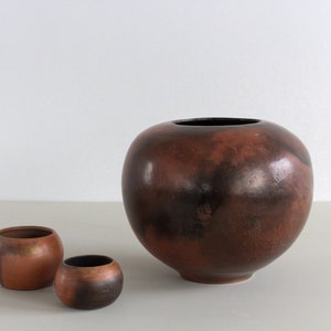 May include: Three ceramic pots, one large and two small. The large pot is brown with black speckles and a round shape. The two smaller pots are also brown with black speckles and a round shape.