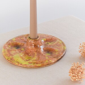 May include: A ceramic candle holder with a yellow and brown glaze. The holder has a round base and a raised centre for a candle.