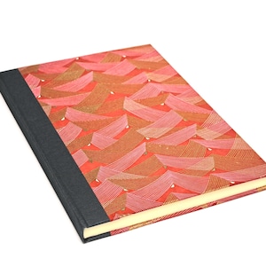 Può includere: Un diario rettangolare con una copertina fantasia. La copertina presenta un design astratto rosso e oro con un dorso nero. Le pagine sono color crema.