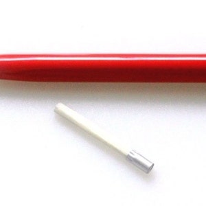 Può includere: Una matita meccanica rossa e nera con una gomma bianca. La matita è lunga circa 15 cm e ha una punta argentata.