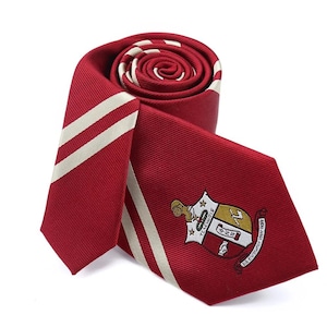 May include: A red silk tie with two white stripes and a gold fraternity crest. The crest features a shield with a lion, a star, and the text "72 NEWCOMBS". The text "The Diamond Tradition" is written on the bottom of the shield.