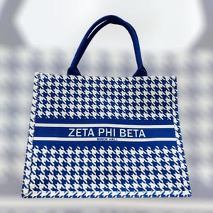 May include: A tote bag with a blue and white houndstooth pattern. The bag has a blue handle and a blue stripe across the front with the text "ZETA PHI BETA MINER HALL".
