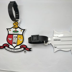 May include: White luggage tag with a black strap. The tag features a red, yellow, and white crest with the text "ΦΣΚ" and "TEARΛΙΩΙS". The tag also has a white space for writing a name, address, and phone number.