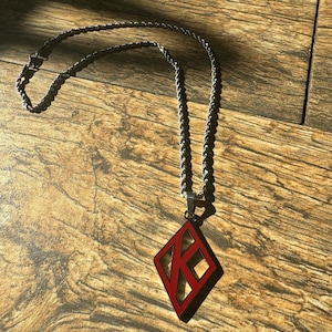May include: A silver chain necklace with a red diamond-shaped pendant featuring a stylized letter K.