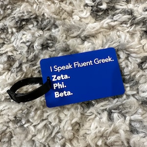 May include: Blue luggage tag with white text that reads "I Speak Fluent Greek."  The tag also has the words "Zeta", "Phi", and "Beta" written on it.