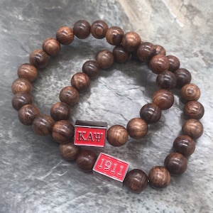 May include: Two brown wooden bead bracelets with red rectangular charms. One charm says "ΚΑΨ" and the other says "1911".