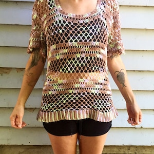 May include: A brown, pink, and green crochet top with a loose fit and short sleeves. The top has a geometric pattern and is semi-transparent.