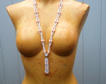 May include: A white and peach beaded necklace with a tassel pendant. The necklace is displayed on a mannequin.