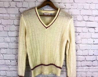 May include: Cream-colored V-neck sweater with long sleeves. The sweater has a ribbed texture and burgundy trim along the neckline, cuffs, and hem. The sweater is hanging on a wooden hanger.