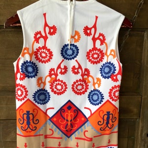 Puede incluir: Top sin mangas blanco con un vibrante estampado geom&eacute;trico en rojo, naranja, azul y beige. El dise&ntilde;o incluye formas florales y de diamante estilizadas. El top tiene una cremallera en la espalda y est&aacute; colgado de una percha de madera.