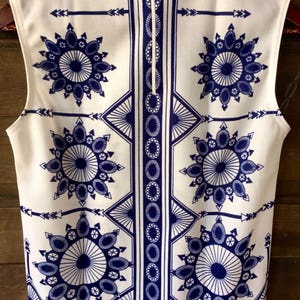 May include: White sleeveless top with a blue and white geometric pattern. The pattern features a repeating design of circles, arrows, and stars.