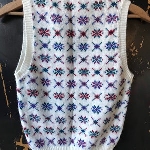 May include: White sleeveless sweater vest with a geometric pattern in red, blue, and green.