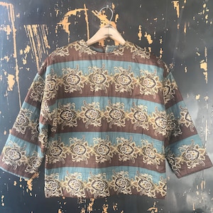 Op de afbeelding: Een bruin en blauw gewatteerd jack met een paisley-patroon. Het jack heeft een losse pasvorm en een ronde hals.