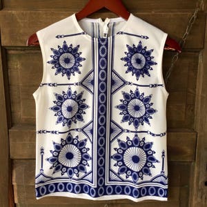 May include: A sleeveless white top with a blue and white geometric pattern. The pattern features repeating circles and arrows.