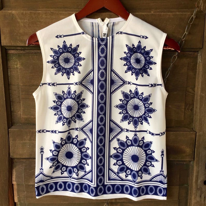 May include: A sleeveless white top with a blue and white geometric pattern. The pattern features repeating circles and arrows.