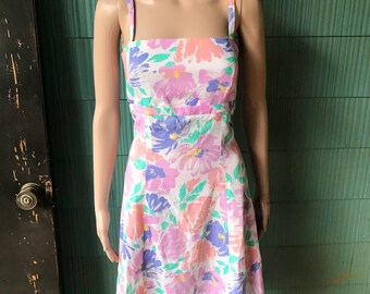 May include: A white sundress with a floral print in shades of pink, purple, and green. The dress has thin straps and a fitted bodice.