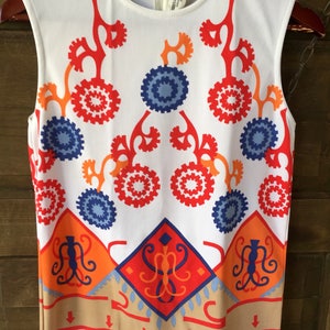 Puede incluir: Top sin mangas blanco con un llamativo dise&ntilde;o geom&eacute;trico en rojo, naranja y azul. El patr&oacute;n incluye formas circulares y de diamante, con un borde beige. El top tiene un cuello redondo y cierre de cremallera.
