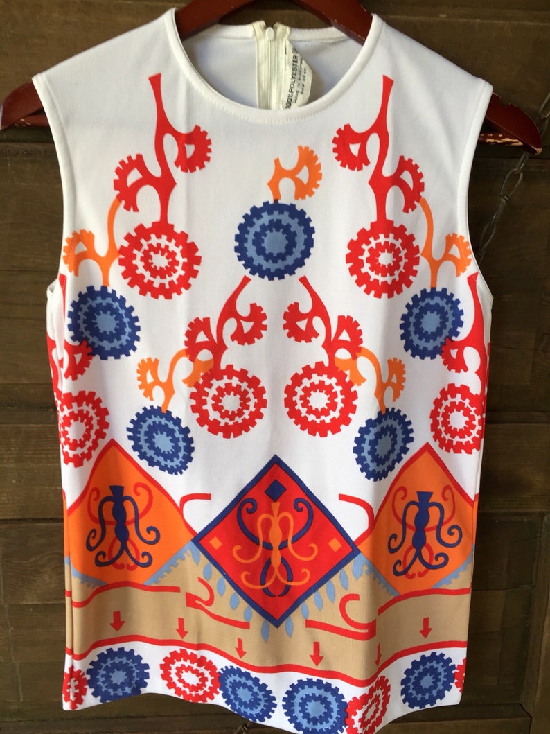 Puede incluir: Top sin mangas blanco con un llamativo dise&ntilde;o geom&eacute;trico en rojo, naranja y azul. El patr&oacute;n incluye formas circulares y de diamante, con un borde beige. El top tiene un cuello redondo y cierre de cremallera.