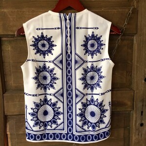 May include: A sleeveless white blouse with a blue and white geometric pattern. The pattern features repeating circles and arrows.