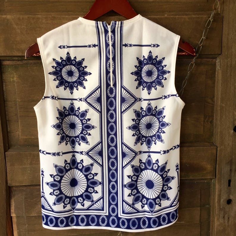 May include: A sleeveless white blouse with a blue and white geometric pattern. The pattern features repeating circles and arrows.
