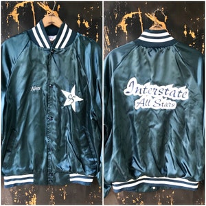 May include: A dark green satin baseball jacket with white and navy blue stripes on the collar and cuffs. The jacket has a button closure and a star with the number 95 on the left side. The back of the jacket has the text "Interstate All Stars" in white lettering.
