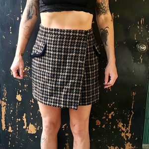 May include: A black and white checked wrap skirt with a black trim. The skirt is knee-length and has a fitted waist.