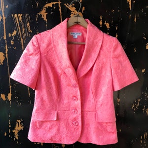 May include: A pink short-sleeved blazer with a floral pattern and a large collar. The blazer has a button closure and two pockets. The label on the blazer reads "Pendleton".