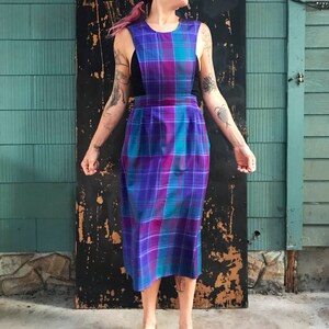 May include: A sleeveless midi dress with a plaid pattern in shades of purple, teal, and pink. The dress has a fitted bodice and a slightly flared skirt.