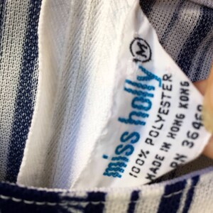 May include: White and blue striped fabric with a white tag that says "miss holly" and "100% POLYESTER" and "MADE IN HONG KONG" and "RN 36460". The tag also has a size "M" in a circle.