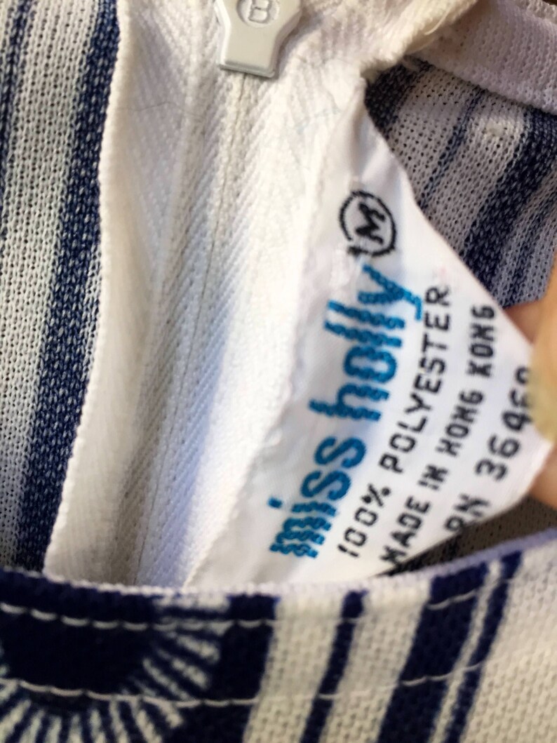 May include: White and blue striped fabric with a white tag that says "miss holly" and "100% POLYESTER" and "MADE IN HONG KONG" and "RN 36460". The tag also has a size "M" in a circle.