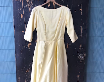 Puede incluir: Un vestido vintage de color amarillo pálido con cuello de barco y mangas tres cuartos. El vestido tiene un corpiño ajustado y una falda completa.