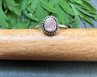 May include: A silver ring with a pink gemstone set in a beaded bezel.