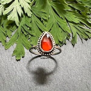 May include: A silver ring with a teardrop-shaped red gemstone set in a beaded bezel.