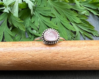 May include: A silver ring with a pink gemstone set in a beaded bezel.